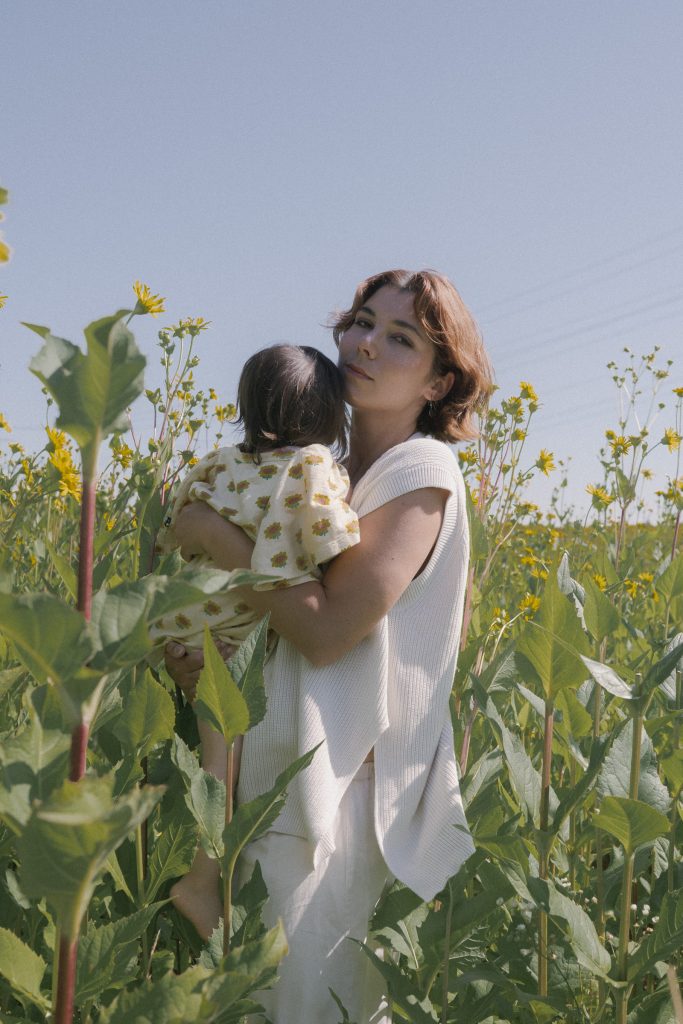 Mutter hält und küsst ihr Kind zwischen hohen Blumen bei einem Outdoor Familienshooting in Freiburg